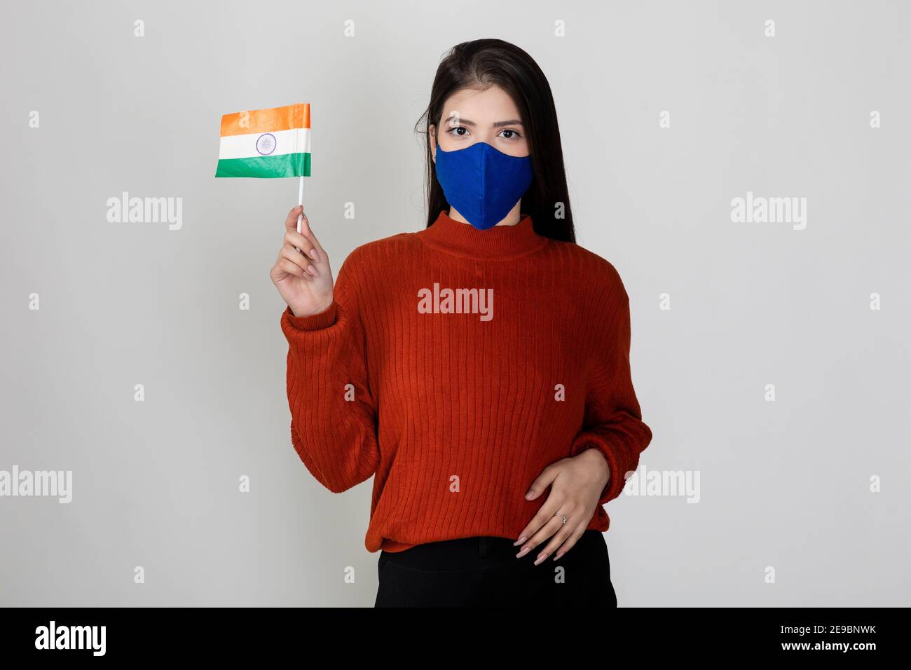 Young beautiful female holding the Indian flag, tricolour on display by pretty woman to show national pride, wearing Covid protection mask. Stock Photo