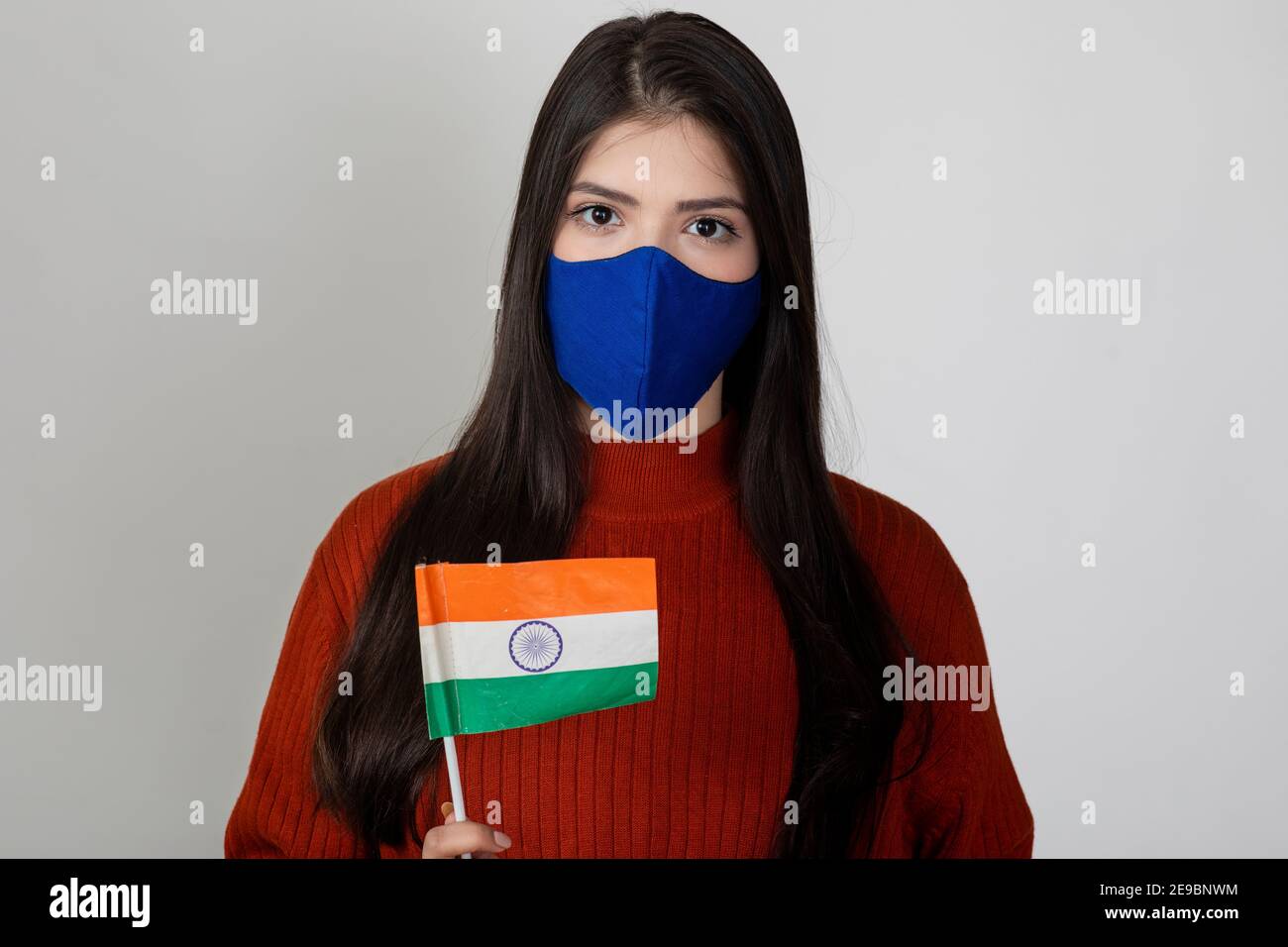 Young beautiful female holding the Indian flag, tricolour on display by pretty woman to show national pride, wearing Covid protection mask. Stock Photo