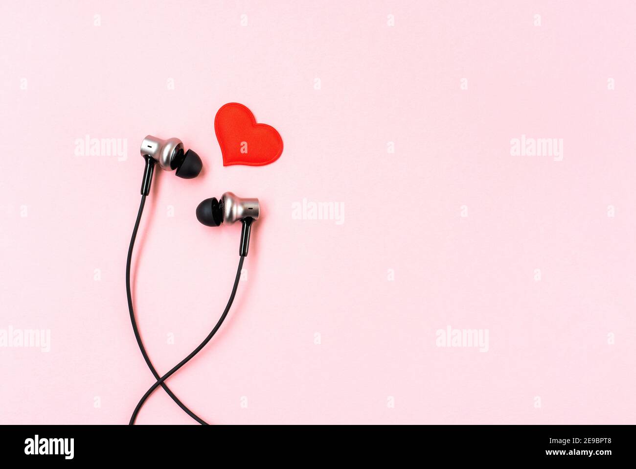 Red heart with music earphones on pink pastel background. Headphones
