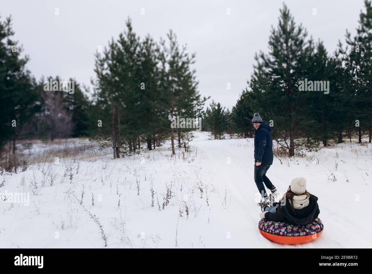 A man in warm winter clothes rolls women on a red tubing.  Stock Photo