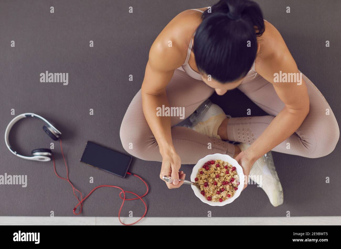 Top view of fit woman sitting on exercise mat and having healthy meal after workout at home Stock Photo