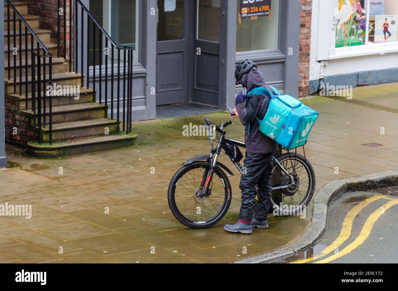 Chester; UK: Jan 29, 2021: A Deliveroo rider checks his mobile phone before starting a delivery. Stock Photo