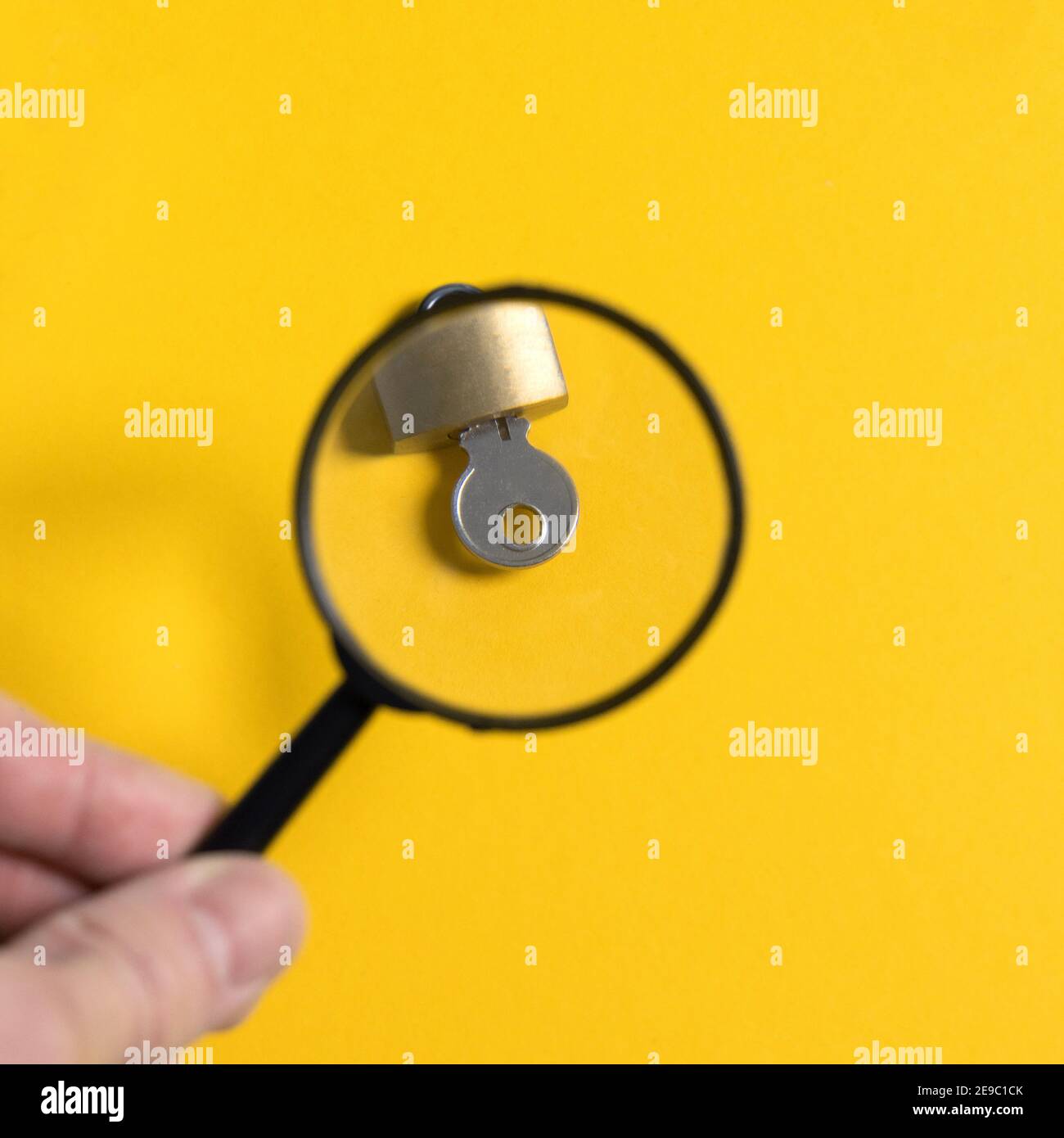hand holding magnifier over key in lock on yellow background. Information privacy concept Stock