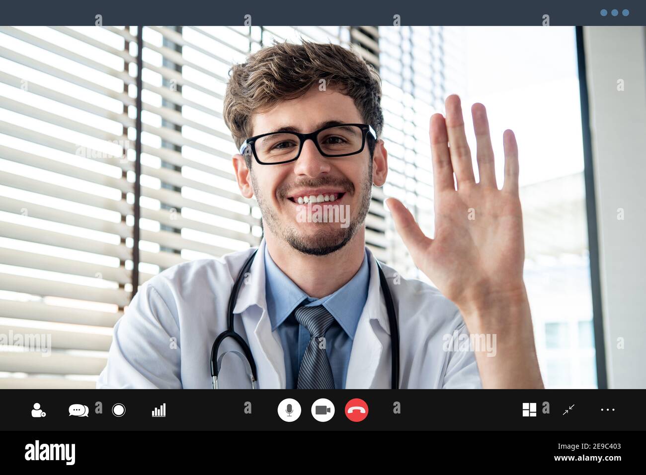Young male doctor waving hand greeting patient online via video call, home medical consulation service concepts Stock Photo