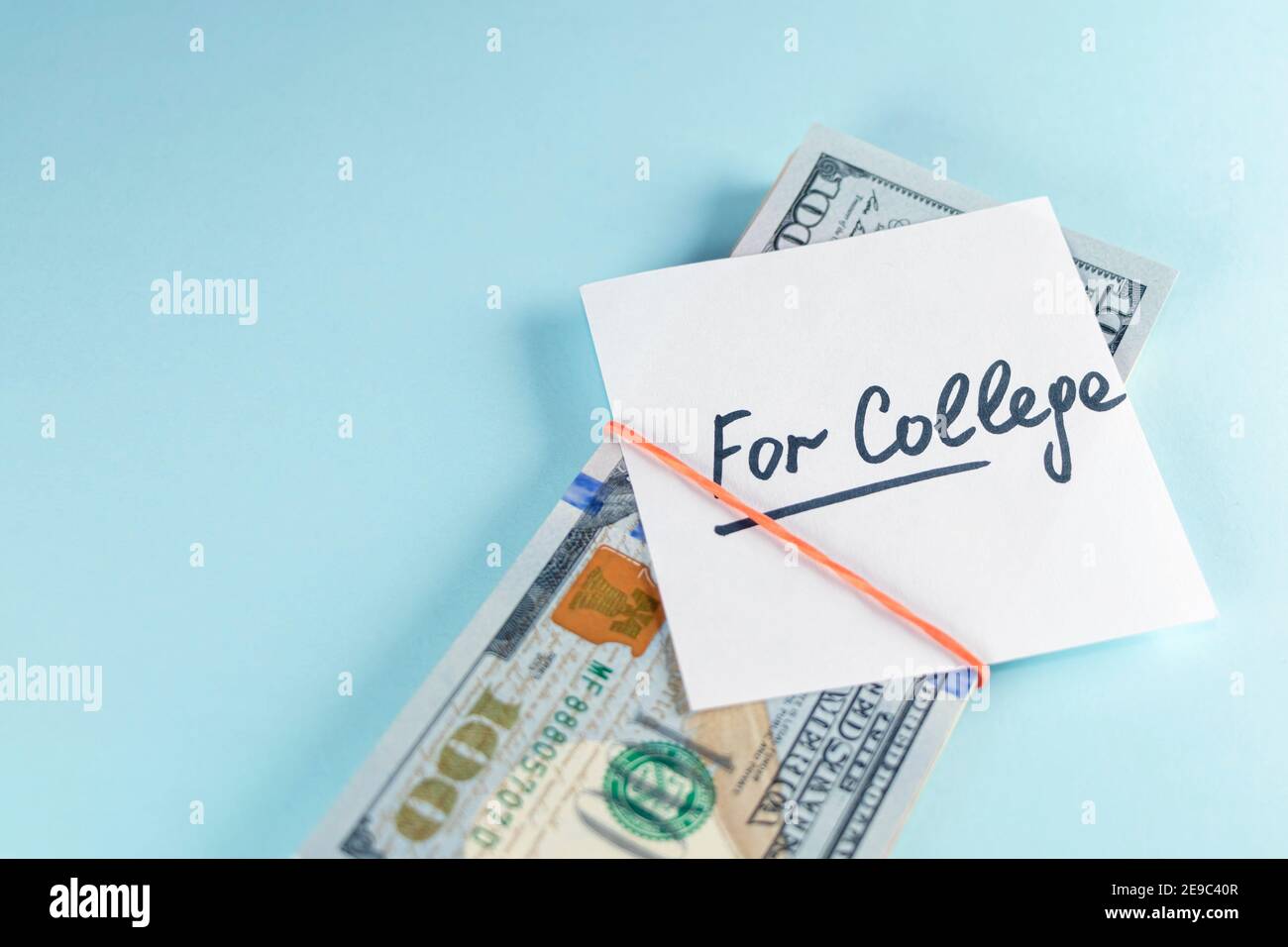 Text written note FOR COLLEGE with dollars cash money in rubber band, on copy space blue background - concept of financial planning to save money for Stock Photo