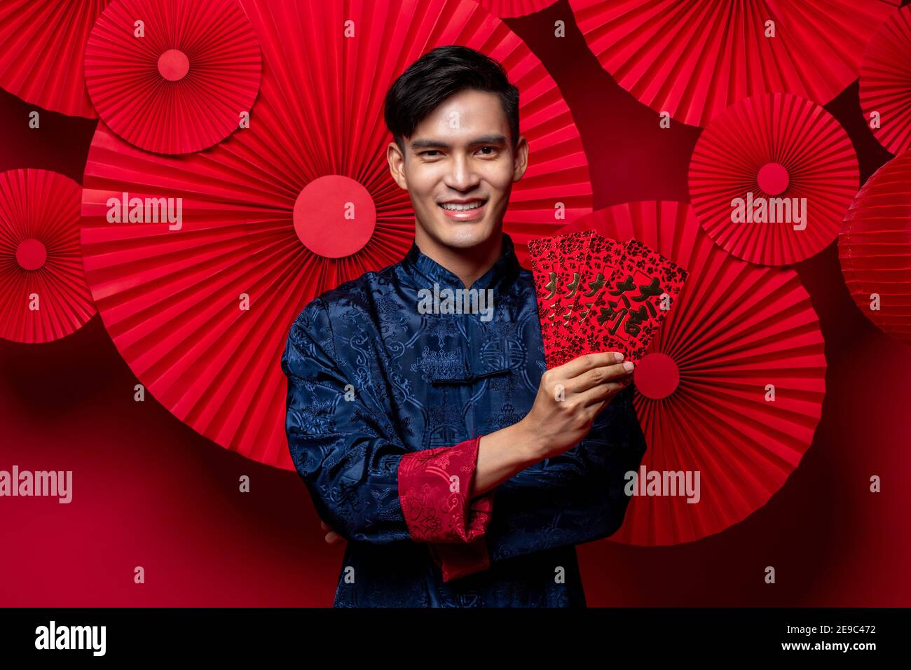 Handsome smiling Asian man in traditional costume holding red envelopes in oriental style folded fan background for Chinese new yaer concepts, text me Stock Photo