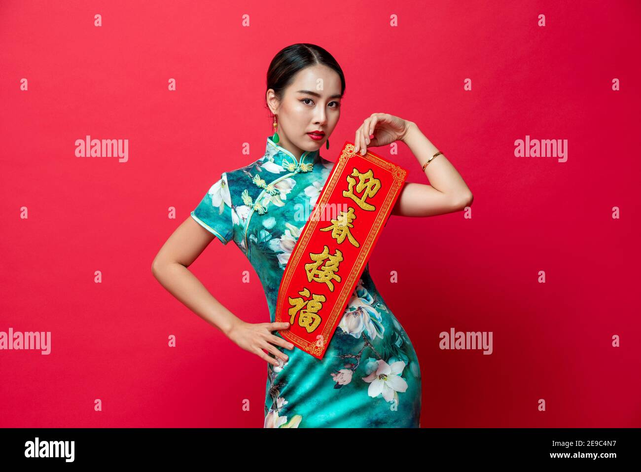 Asian woman wearing oriental cheongsam dress presenting Chinese new year label in red isolated studio background, text means wishing of prosperity Stock Photo