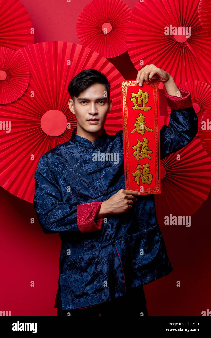 Handsome Asian man in traditional costume holding lebal in red oriental decoration background for Chinese new yaer concepts, text means wishing of pro Stock Photo