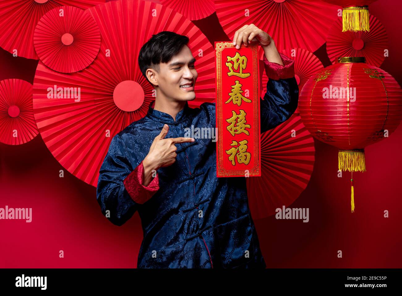 Handsome smiling Asian man in traditional costume holding and pointing to lebal in red oriental decoration background for Chinese new yaer concepts, t Stock Photo