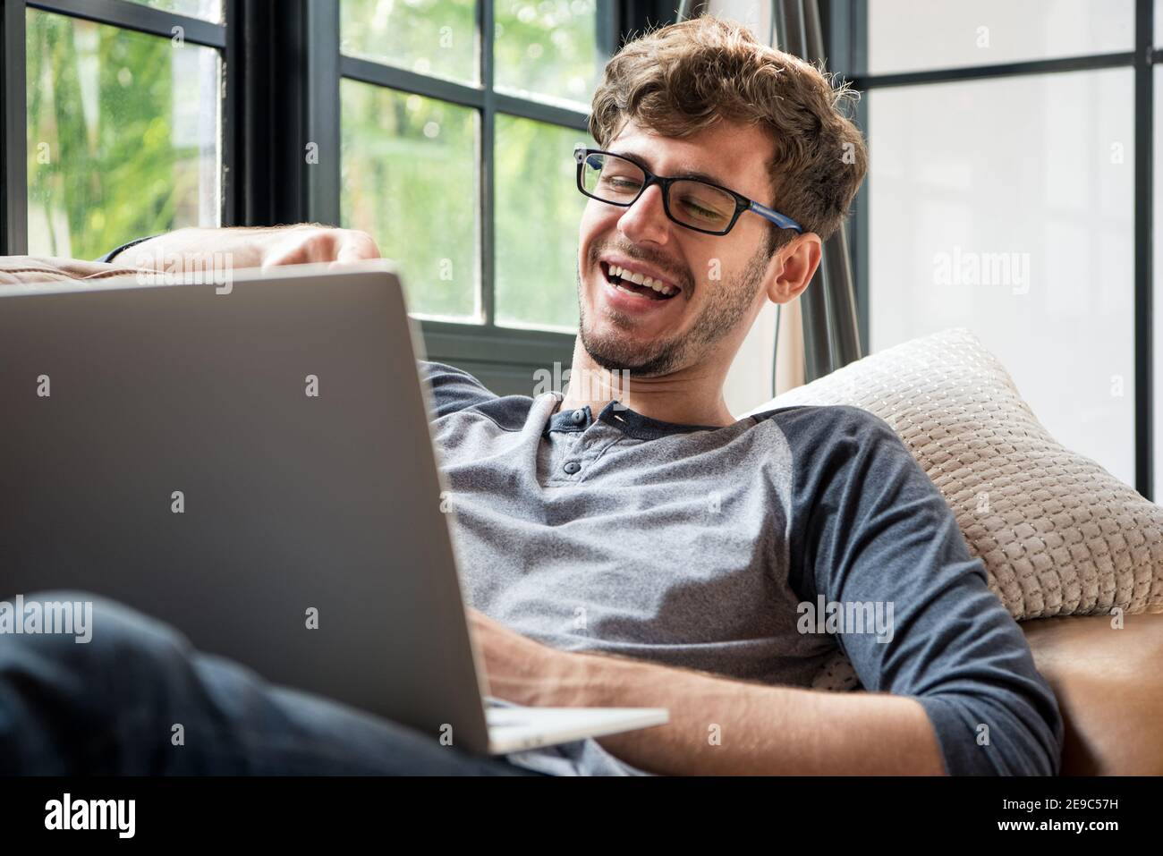 Young happy Caucasian man laughing while making video call chatting online with laptop computer on the couch at home Stock Photo