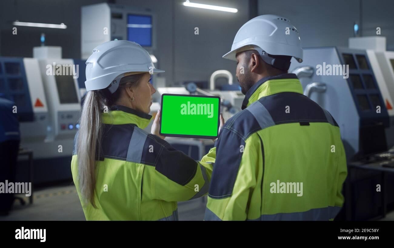 Industry 4.0 Factory: Chief Engineer and Project Supervisor in Safety Vests and Hard Hats, Talk, Use Digital Tablet Computer with Green Screen, Chroma Stock Photo