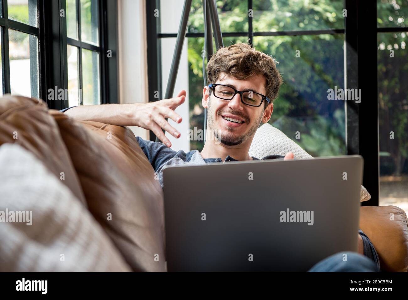 Young happy Caucasian man chatting online via video call with laptop computer on the couch at home Stock Photo