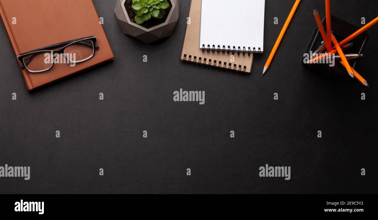 Office desk with supplies and potted plant over black leather table. Top view flat lay with copy