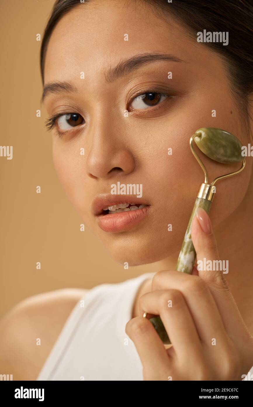 Close Up Portrait Of Beautiful Young Woman Looking At Camera And Using Jade Roller For Massaging