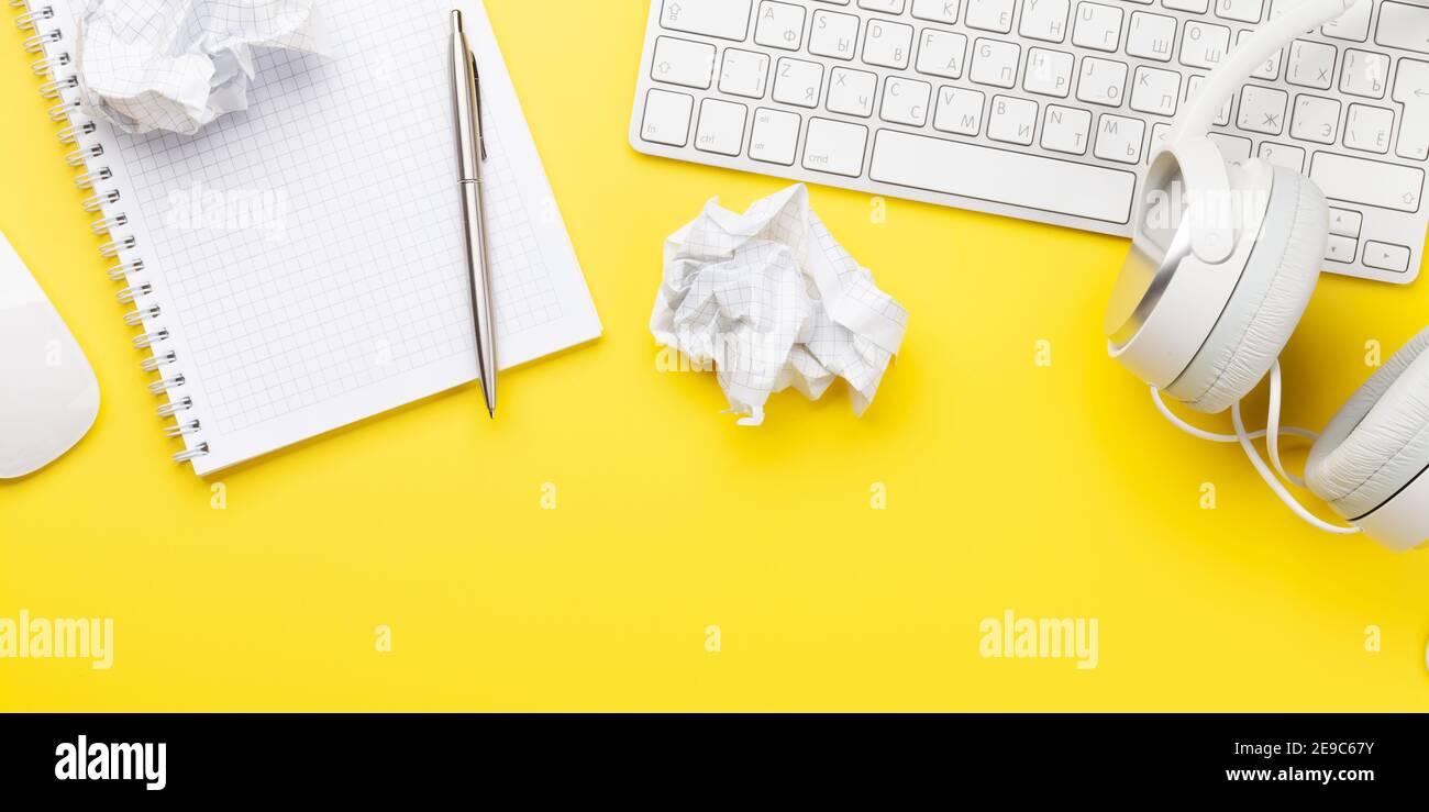 Office desk with supplies, headphones and blank notepad over yellow. Creativity and inspiration