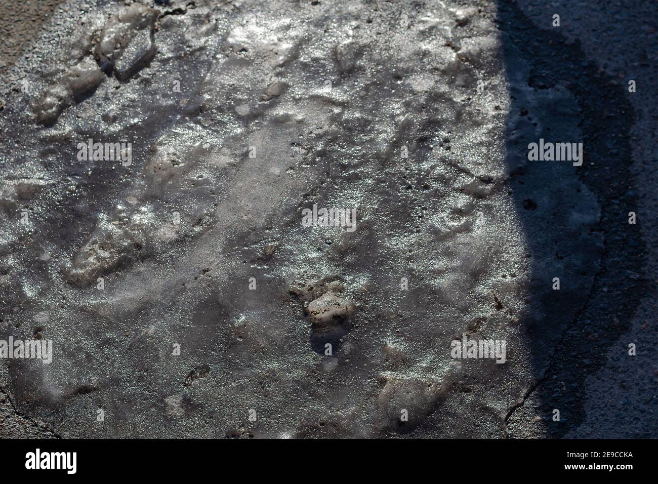 Frozen puddle of water in the street on the pavement. The texture of ...
