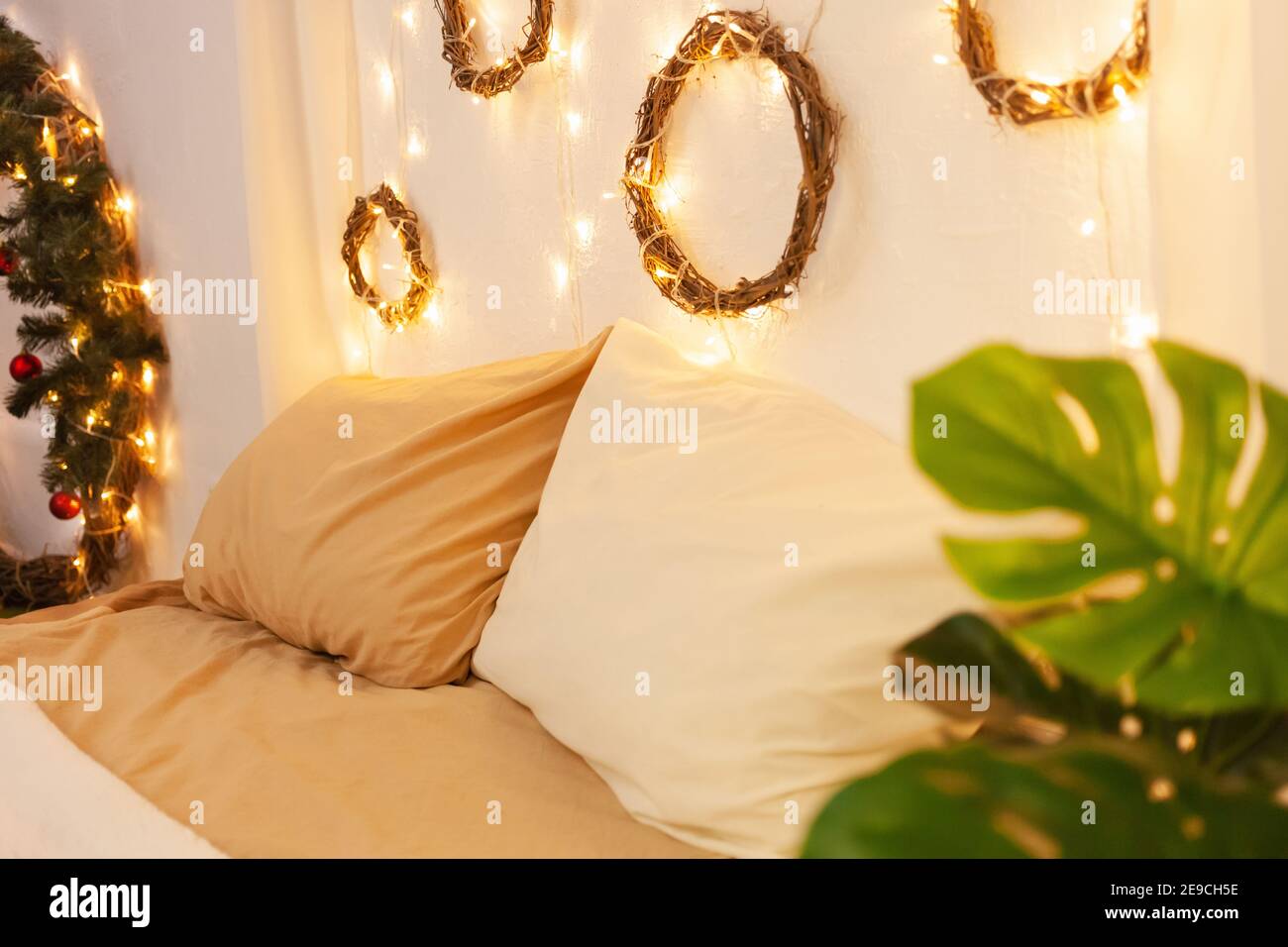 https://c8.alamy.com/comp/2E9CH5E/christmas-photo-zone-bedroom-bed-with-two-pillows-home-monstera-plant-the-walls-are-decorated-with-new-years-wreaths-of-branches-and-lights-yell-2E9CH5E.jpg