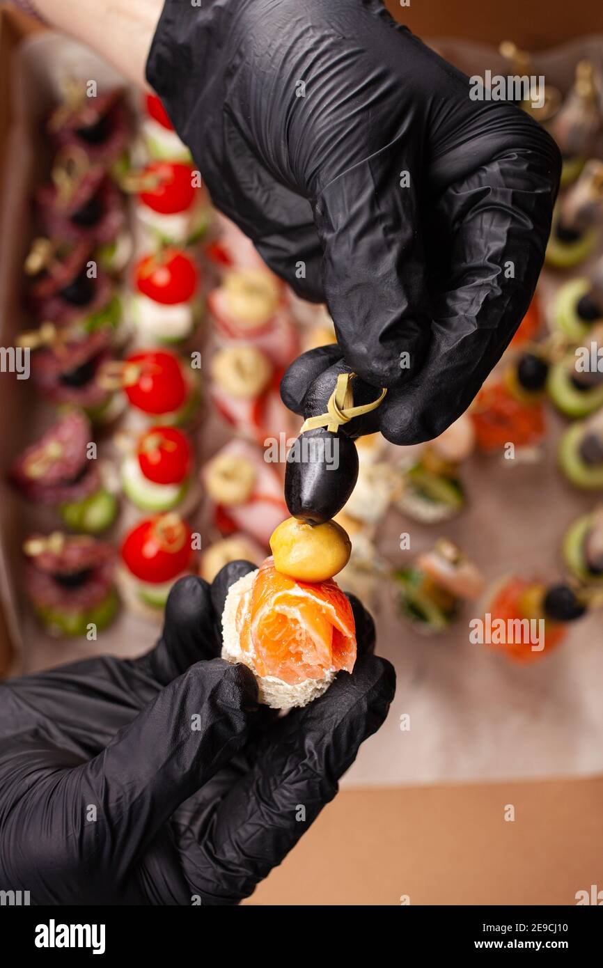 Canape, hands in black gloves hold a beautiful canape on a cap. Catering, snacking, beautiful food. Studio photo. Stock Photo