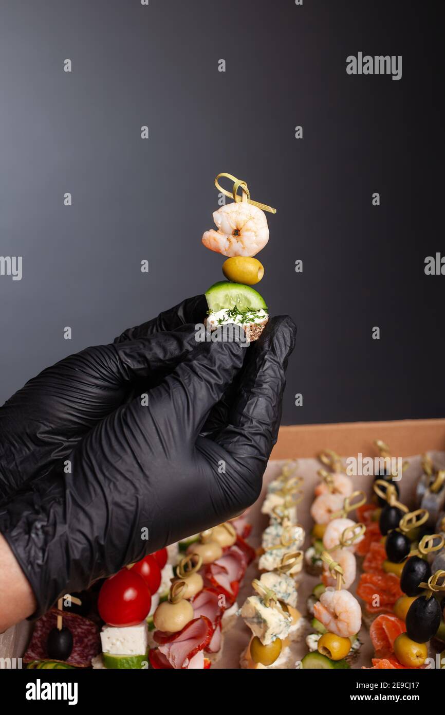 Canape, hands in black gloves hold a beautiful canape on a cap. Catering, snacking, beautiful food. Studio photo. Stock Photo