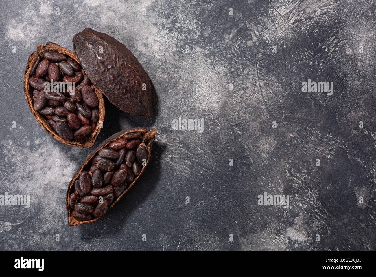 Split fermented cocoa pods with shelled cacao beans atop dark grey backdrop, top view, copy space Stock Photo