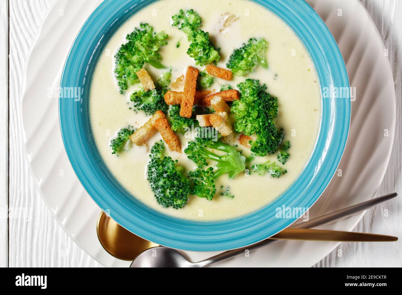 cream soup with broccoli and croutons in a blue bowl on a white wooden ...