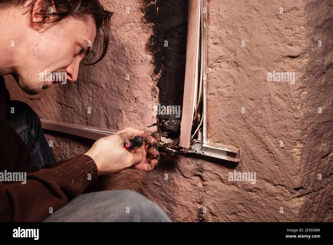 A man fixes a burnt socket. Short circuit, burnt wires. traces of smoke