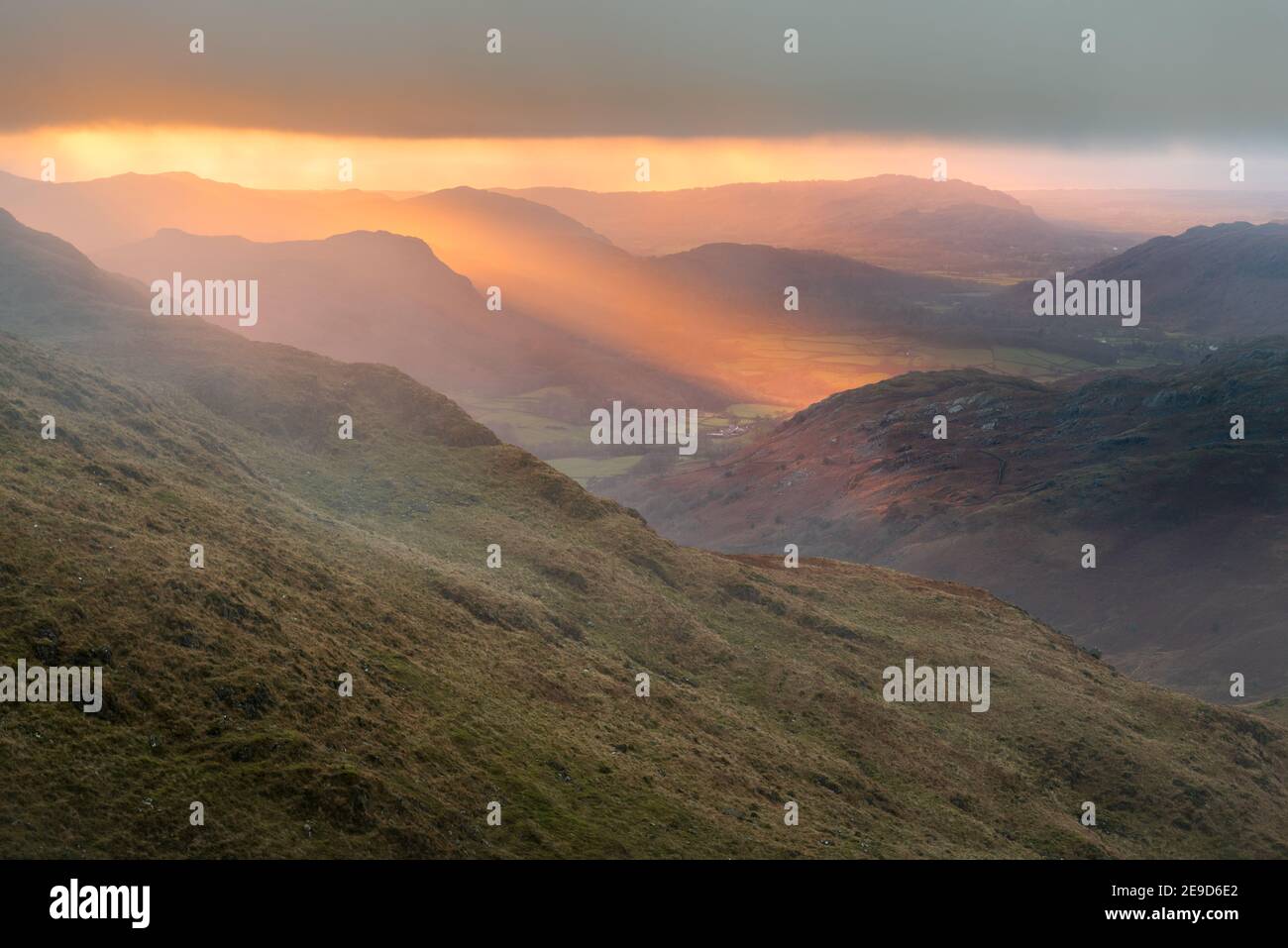 Golden evening light at sunset breaking through clouds onto mountains. Eskdale Valley in the English Lake District. Stock Photo