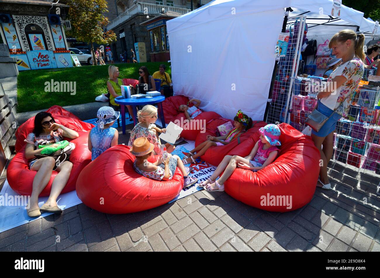 Children and women sitting on beanbag chairs in a street lounge zone, reading books Stock Photo