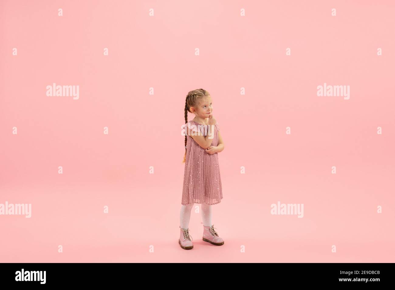Hopeful. Childhood and dream about big and famous future. Pretty longhair girl on coral pink studio background. Childhood, dreams, imagination, education, facial expression, emotions concept. Stock Photo