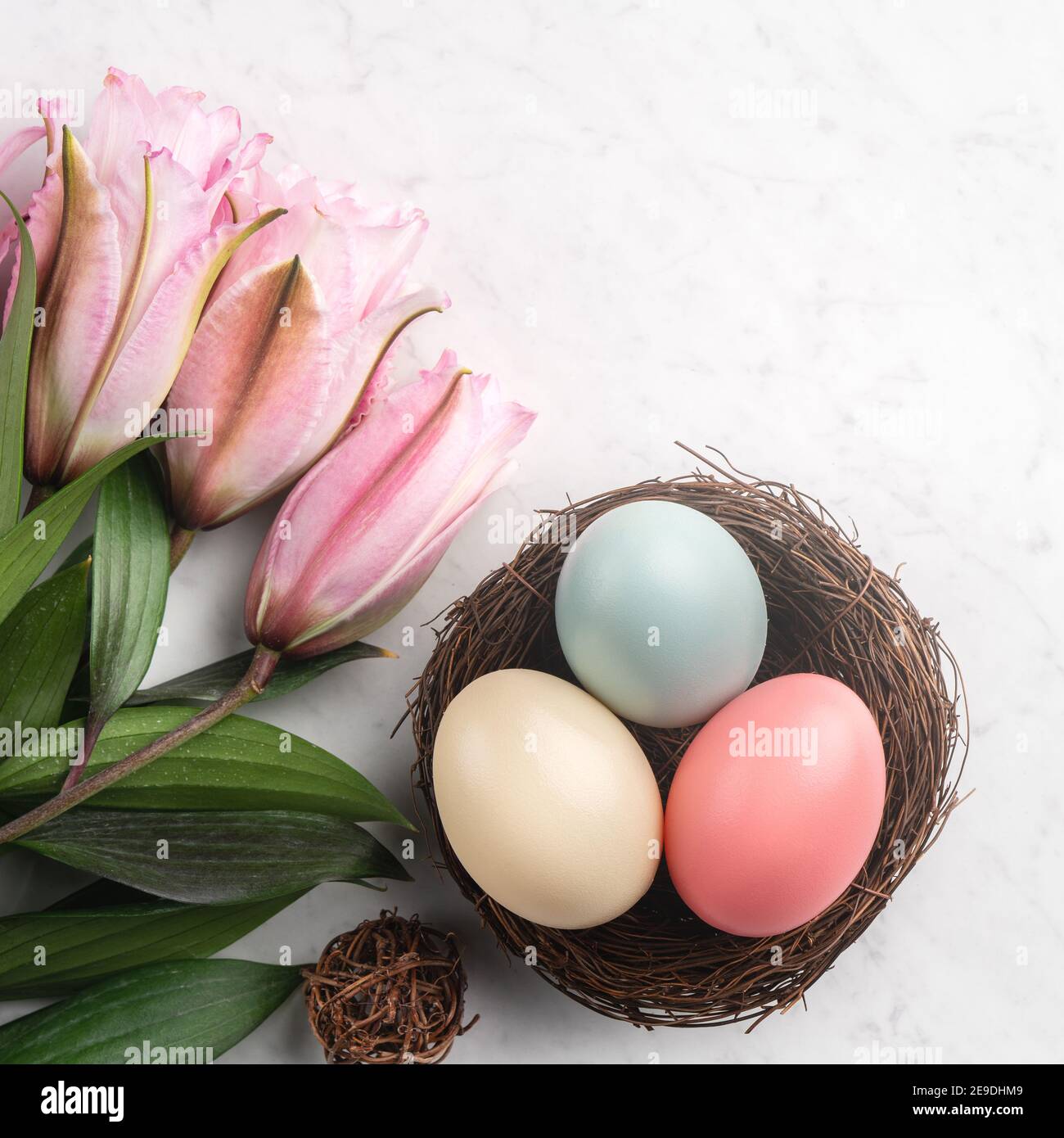 Colorful Easter eggs in the nest with pink lily flower on bright marble ...