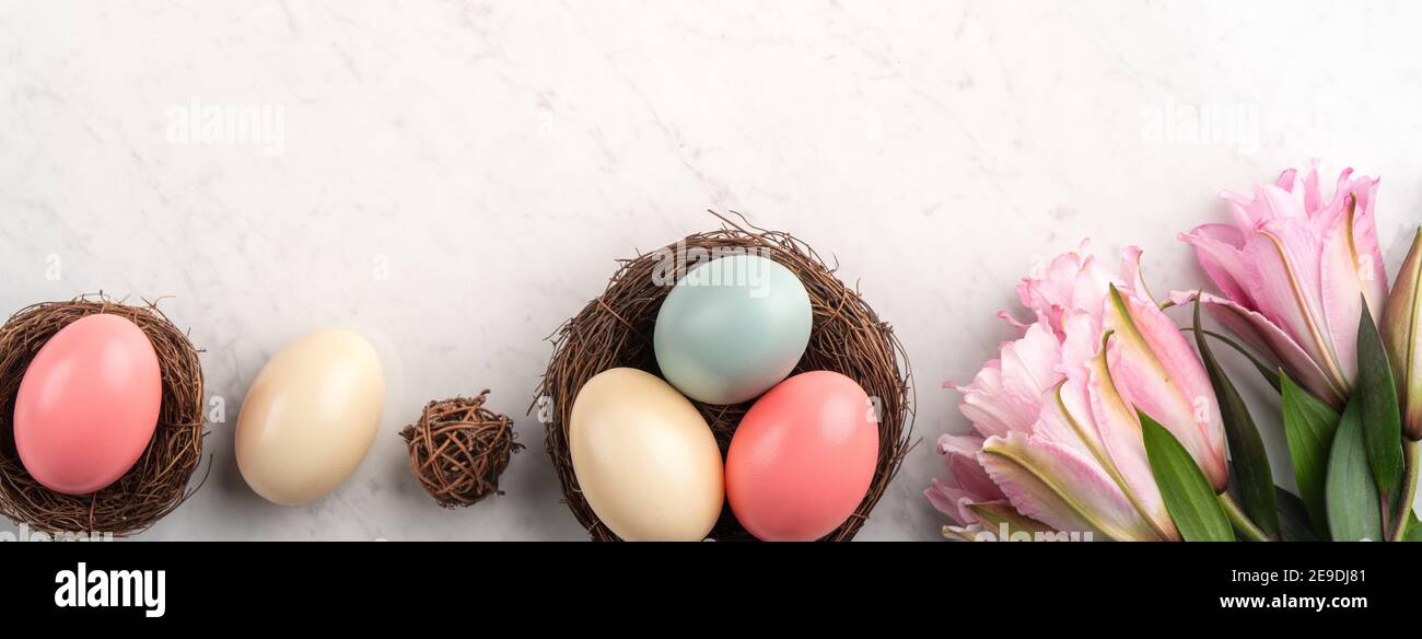 Colorful Easter eggs in the nest with pink lily flower on bright marble ...