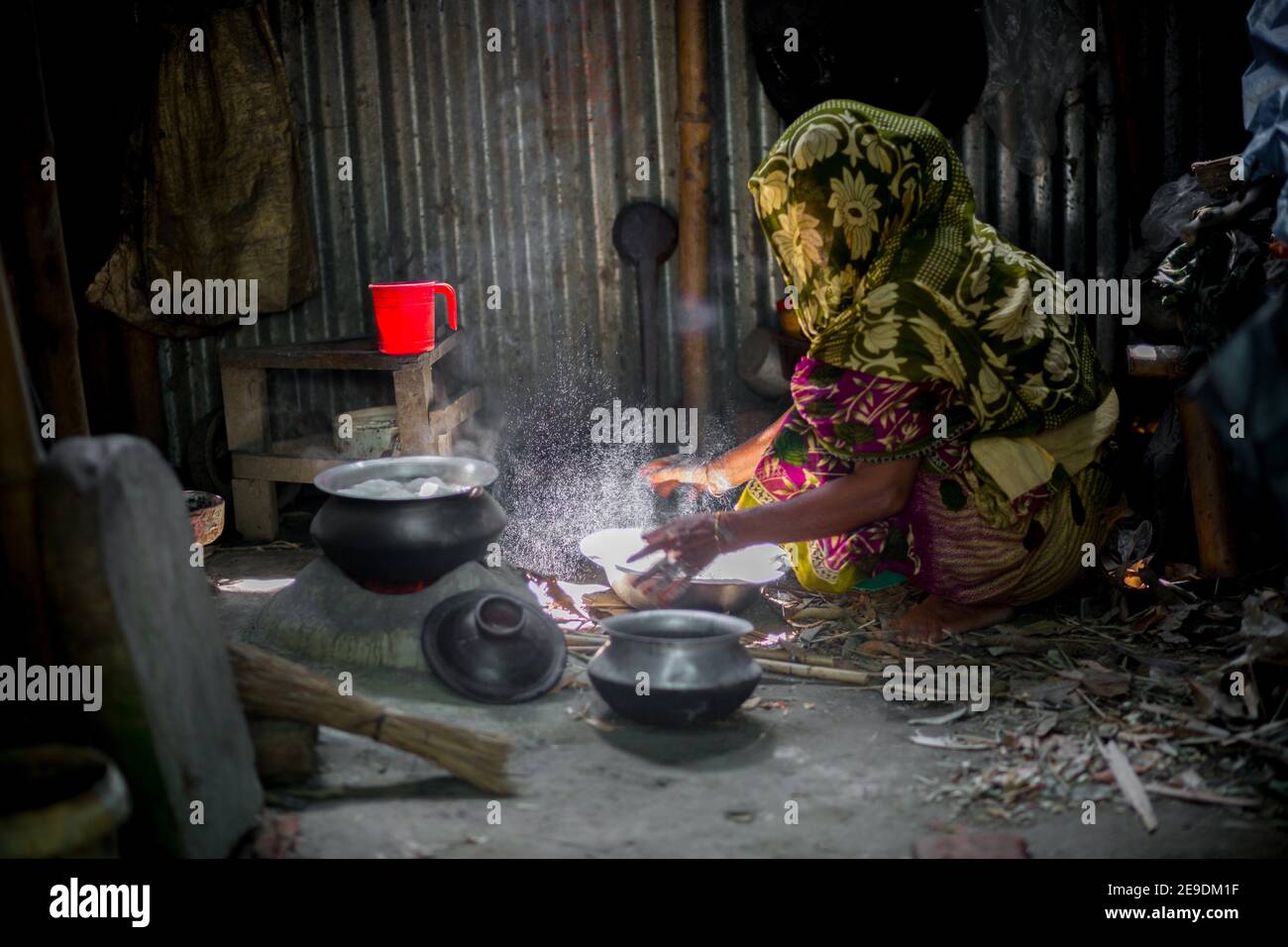 A woman is cooking rice balls on a traditional charcoal-burning clay stove at Narsingdi, Bangladesh. Stock Photo