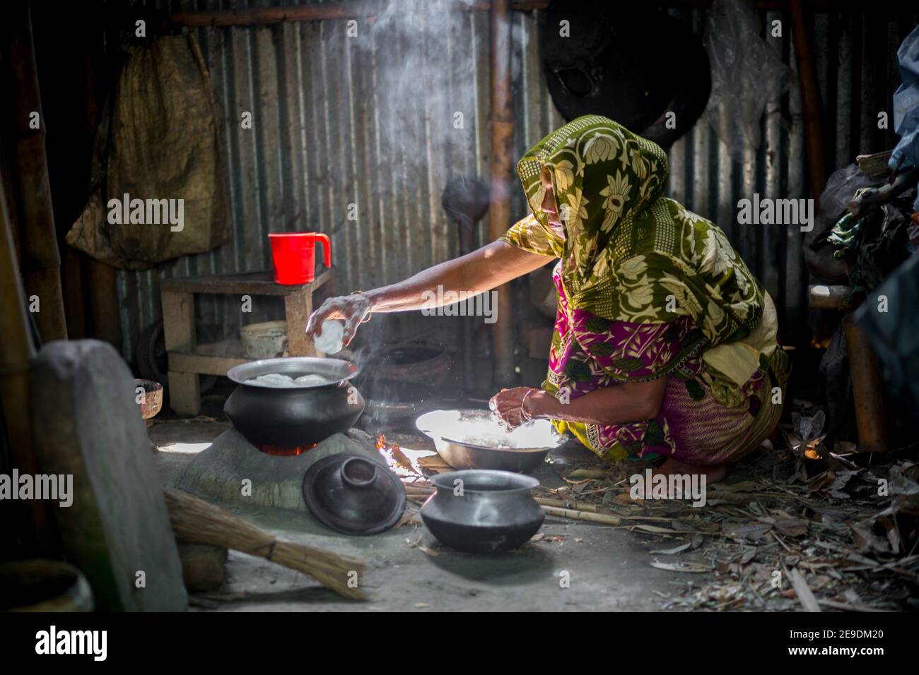 A woman is cooking rice balls on a traditional charcoal-burning clay stove at Narsingdi, Bangladesh. Stock Photo