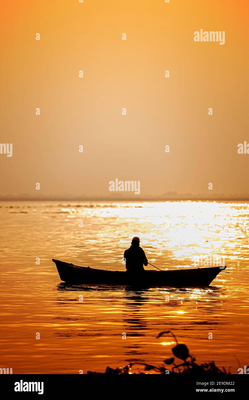 Evening golden sunset time, a fisherman fishing on the seaside on a boat. Stock Photo