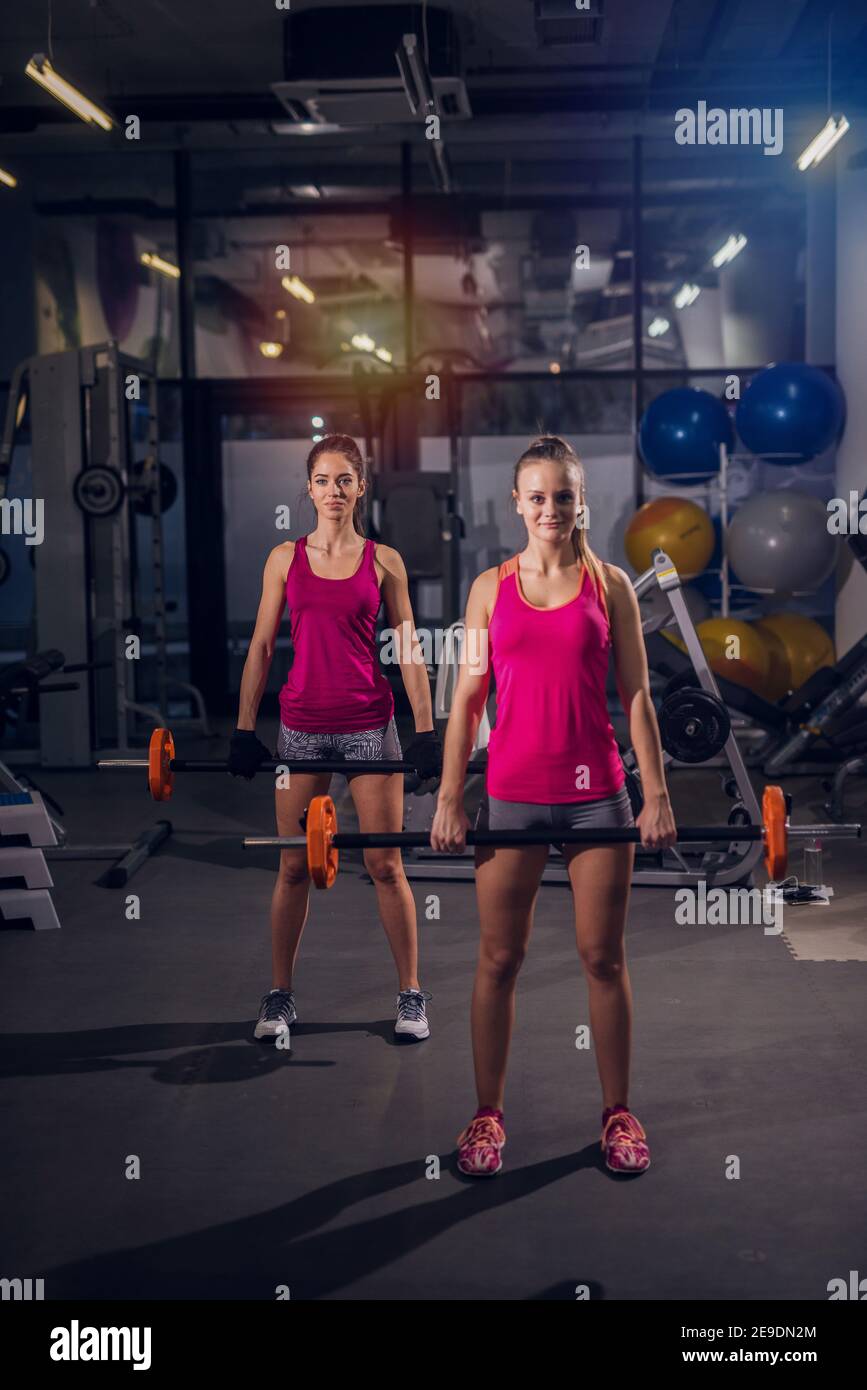 Two strong young girls in a gym holding heavy bars and looking at the camera. Stock Photo