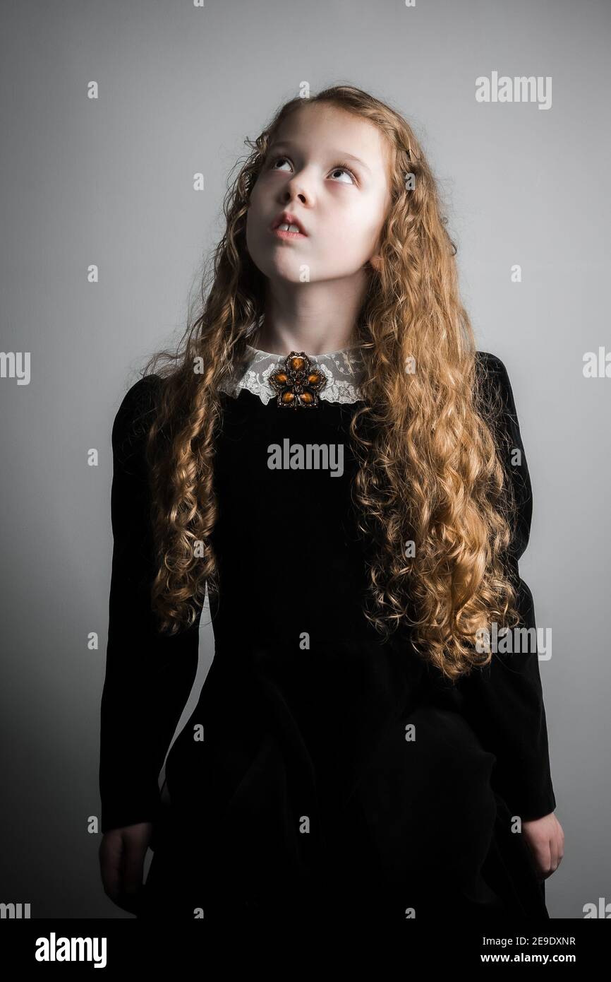 Beautiful young girl in black 1890s English Victorian 18th century child period velvet dress with elegant white lace collar antique broach looking up Stock Photo