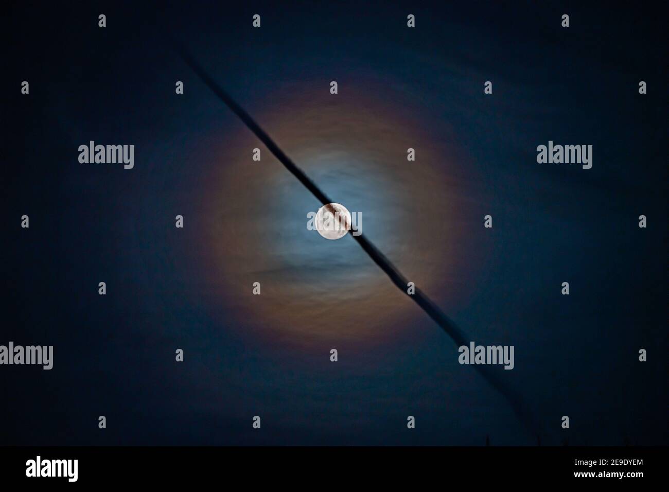 Lunar corona with jet vapour trail crossing in front Stock Photo