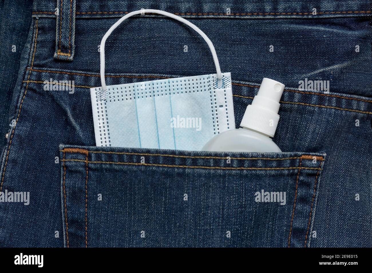 Protective face mask and hand sanitizer spray is lying in back pocket of blue jeans. Concept for new lifestyle after COVID-19 coronavirus pandemic. Stock Photo