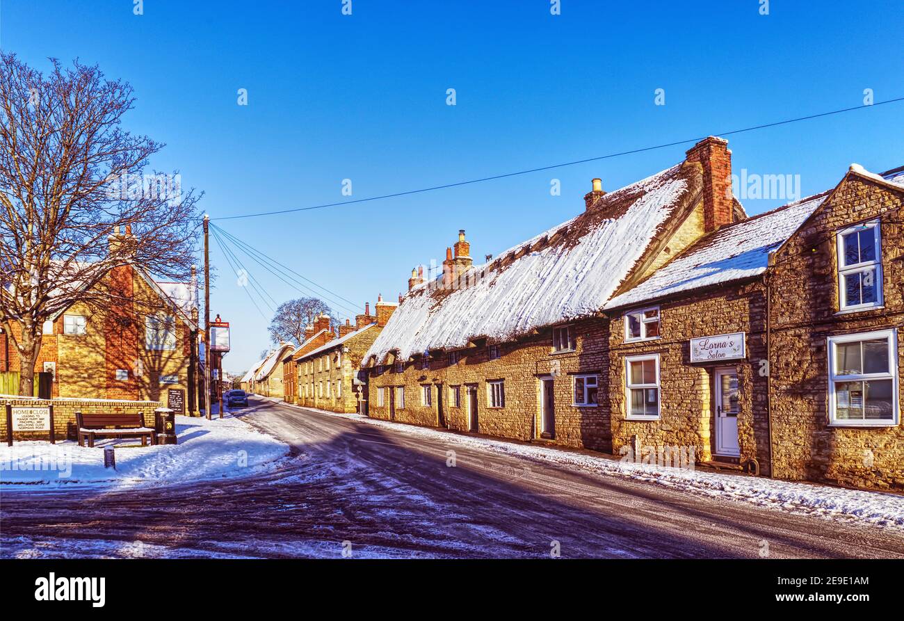 Sharnbrook, Bedfordshire, England, UK - Sharnbrook village high street winter scene after snow with hairdressers shop, pub and thatched cottages Stock Photo