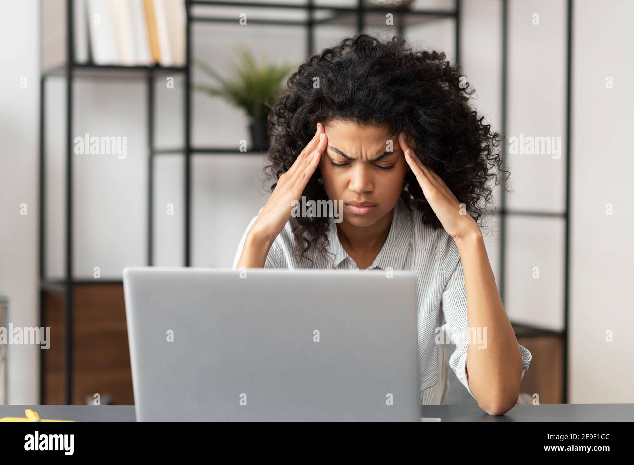 Exhausted millennial African American businesswoman female office worker touching massaging temples suffering from severe headache or migraine, tired Stock Photo