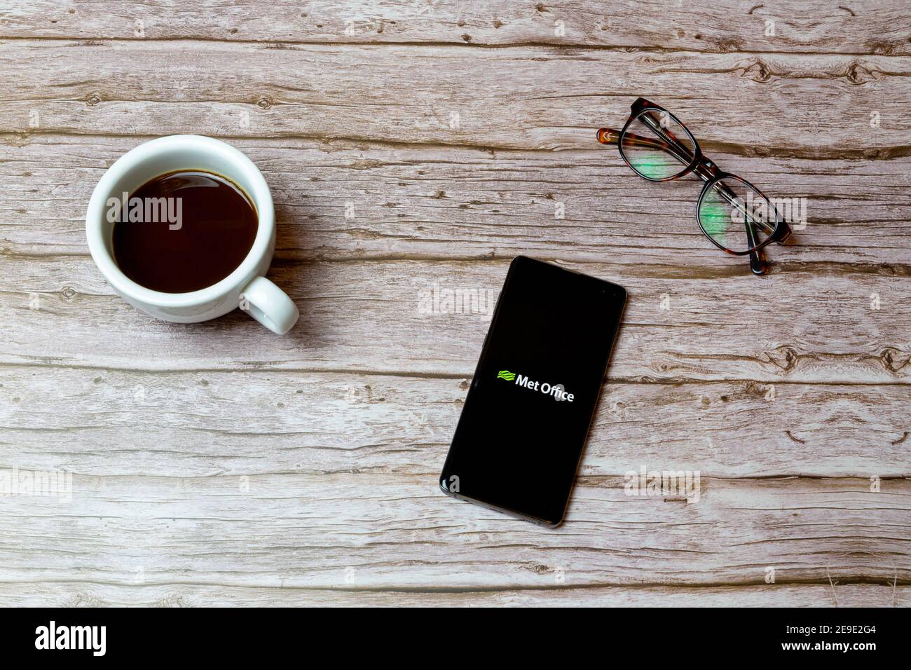 A Mobile phone or cell phone laid on a table or desk with the Met Office weather app open and a coffee next to it Stock Photo