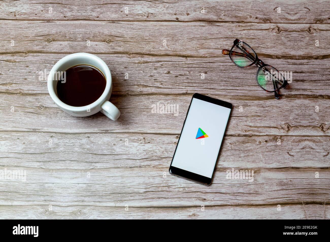 A Mobile phone or cell phone laid on a table or desk with the Google play store app open and a coffee next to it Stock Photo