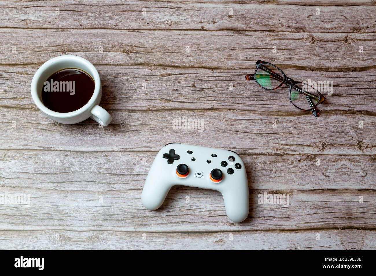 A google Stadia games contoller laid on a desk or table next to a coffee and glasses Stock Photo