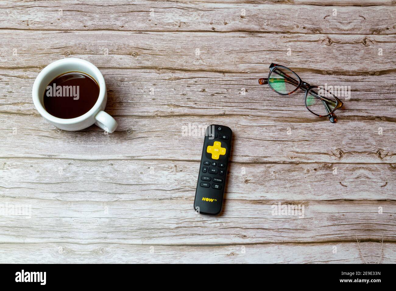 02-04-2021 Portsmouth, Hampshire, UK A Yellow Now TV remote control laid on a table or desk next to glasses and a coffee Stock Photo