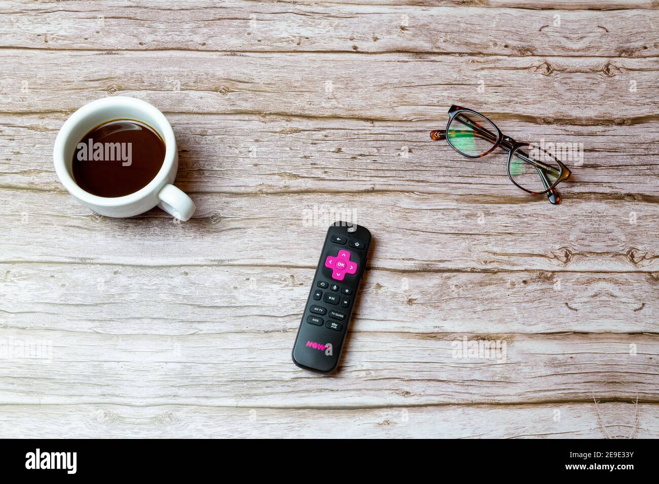 02-04-2021 Portsmouth, Hampshire, UK A Pink Now TV remote control laid on a table or desk next to glasses and a coffee Stock Photo