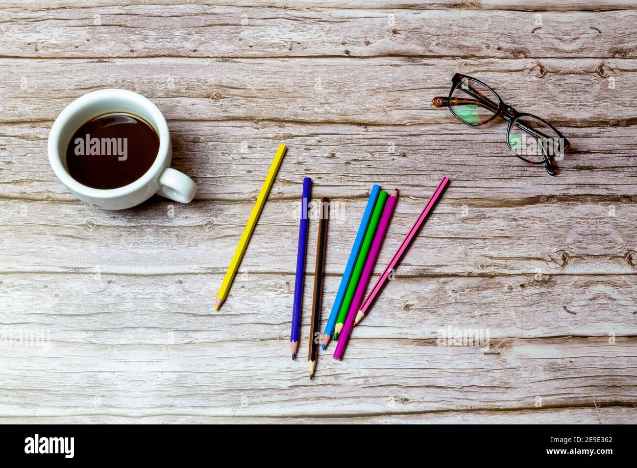 Various colour colouring pencils on a wooden desk or table next to a coffee and glasses Stock Photo
