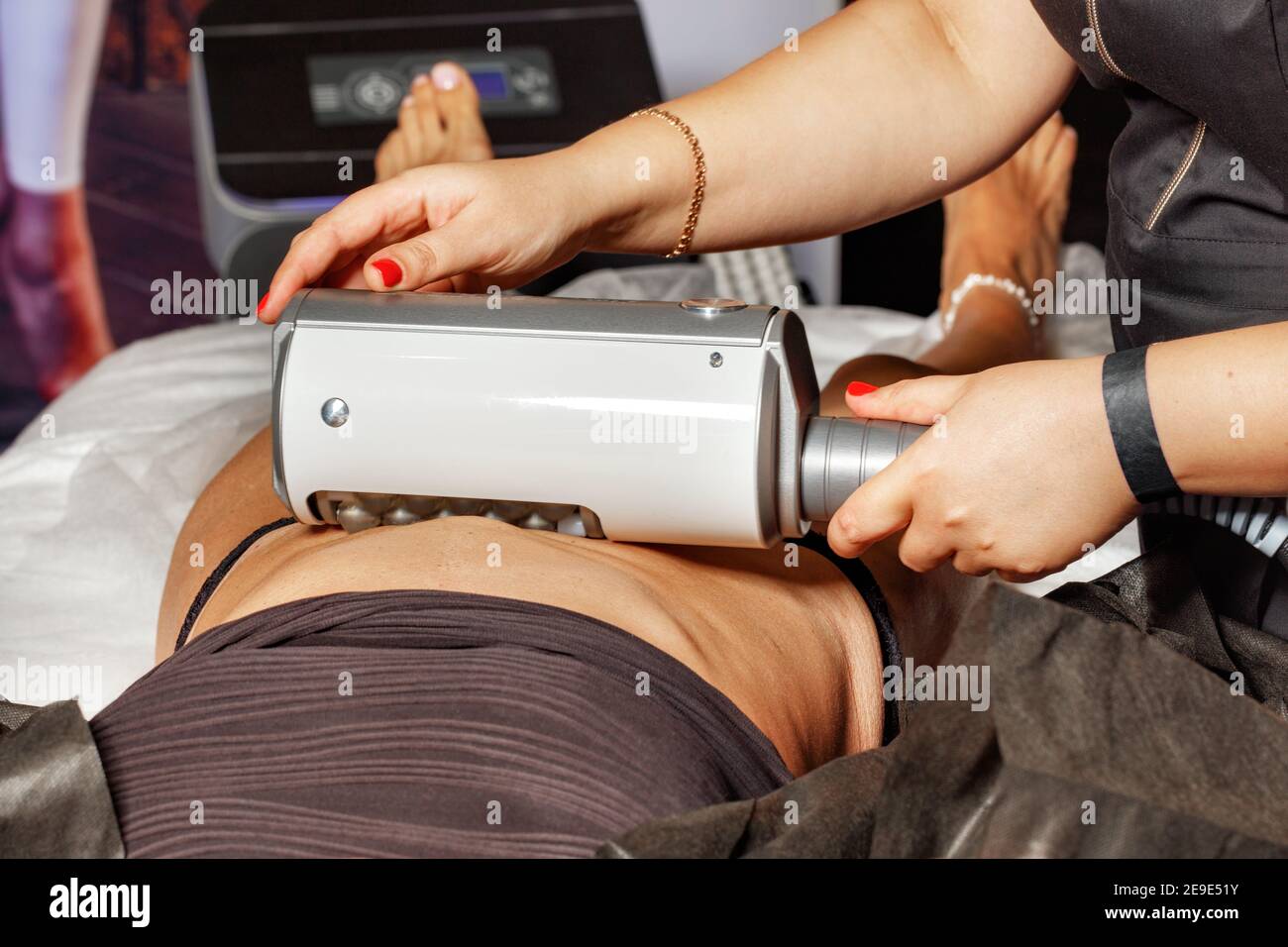 A professional cosmetologist performs an electromagnetic massage of the abdominal muscles on a woman patient on a high-intensity simulator. Stock Photo