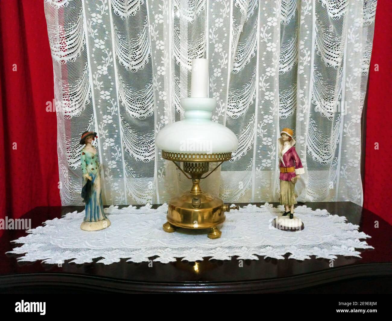 old brass kerosene stove transformed into an electric lamp flanked by figurines with a lace curtain Stock Photo