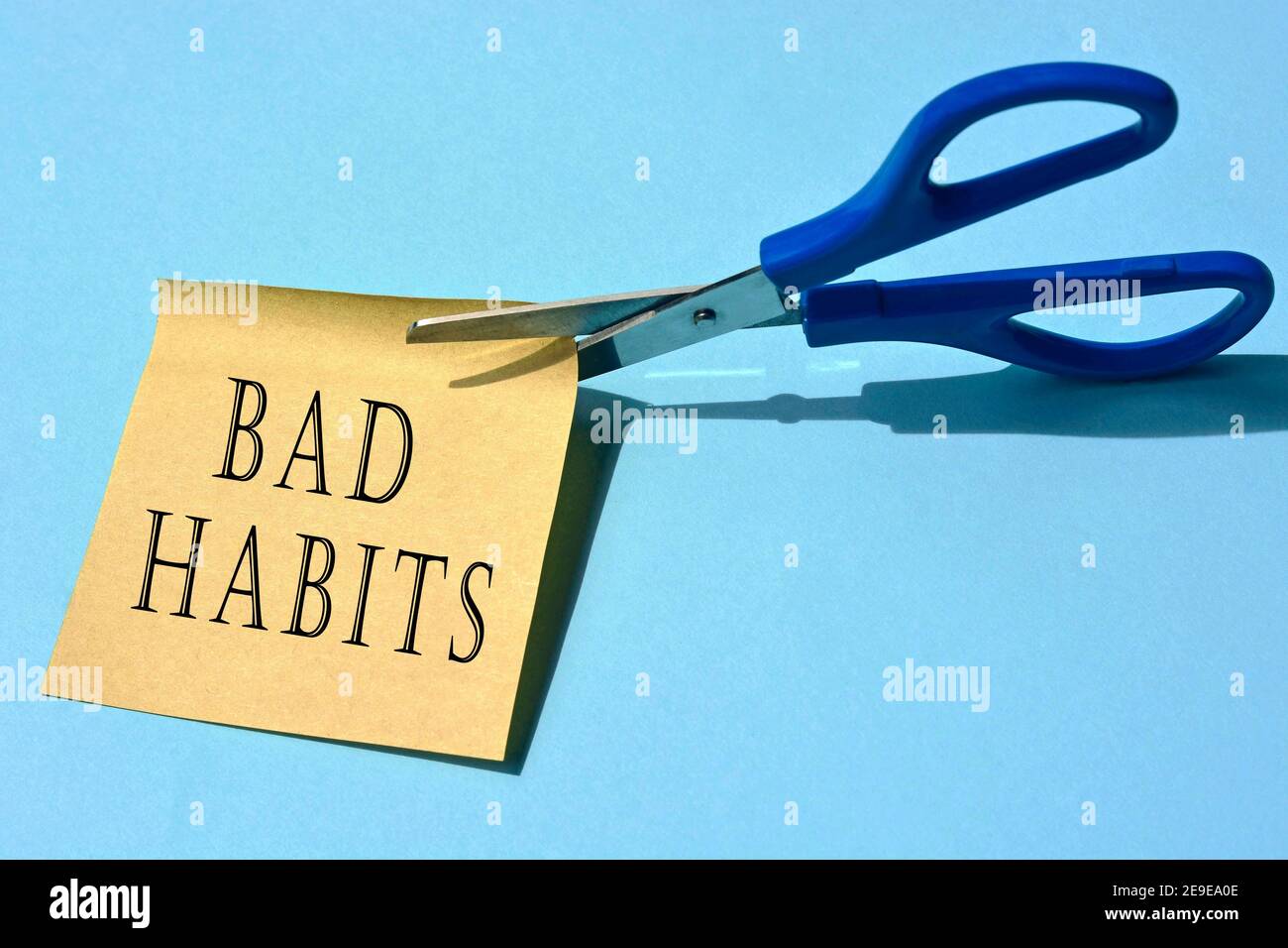 Scissors that cut yellow notepad with bad habits text on a blue background. Stock Photo