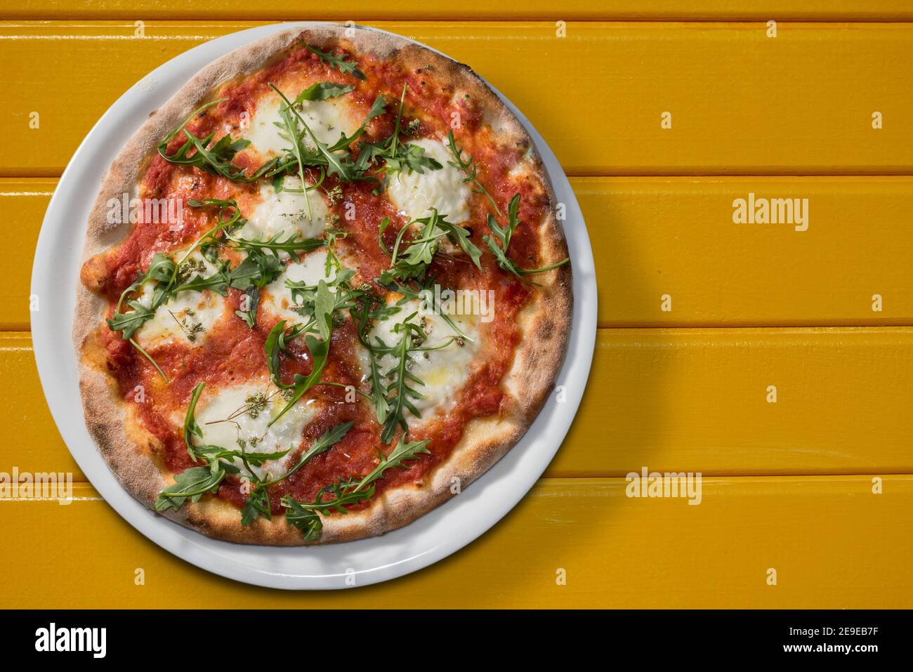 Pizza with tomato sauce, mozzarella and arugula or rocket in white plate on yellow boards, flat lay in top view with copy space Stock Photo